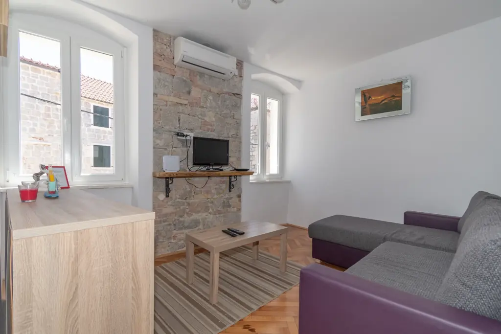 Dnevni boravak s kaučem na razvlačenje, TV-om i kamenim zidom, apartman Kira Split